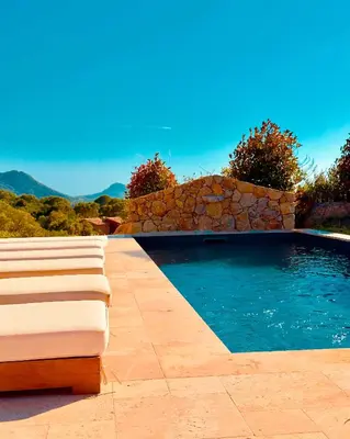 a swimming pool with two chaise lounges next to a stone wall at Domaine Aria di Terra***** in Figari