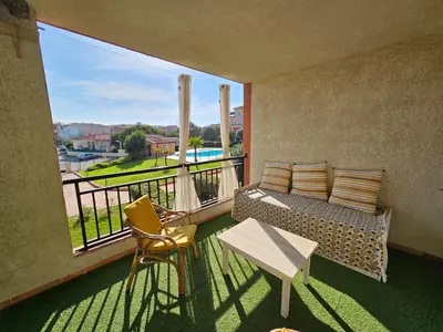 a balcony with a couch and a table and chairs at Palmeraie 406- vue piscine- clim- proche plage et commerces in Sari Solenzara