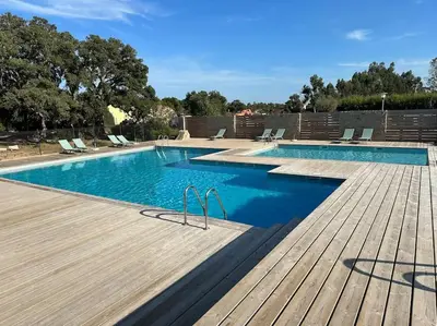 a swimming pool with a wooden deck and blue water at Mini villa T3 de 48m2 in Lecci