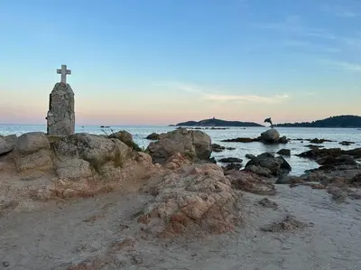 a cross on the beach with rocks and a lighthouse at Mini villa T3 de 48m2 in Lecci