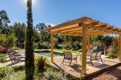 a wooden deck with chairs and a pergola in a garden at Lodge La Myrte Di Lecci in Lecci