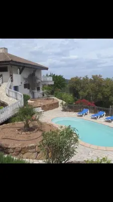 a swimming pool with two blue chairs next to a house at Maison Le Guetali in Zonza