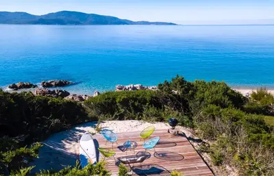 a wooden deck with chairs and tables on the beach at The Beach House in Olmeto