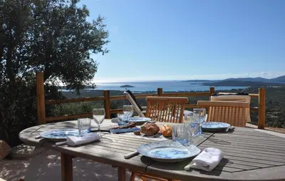 a wooden table with plates and glasses on a deck at Appartement RDJ ds villa vue mer panoramique in Lecci