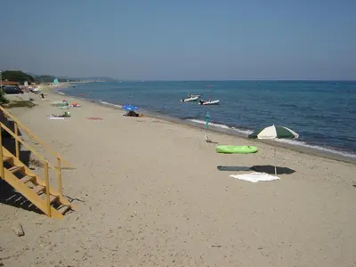 a beach with umbrellas and people in the water at Graziosa villetta in residence con piscina a 100 m dalla spiaggia in Cervione