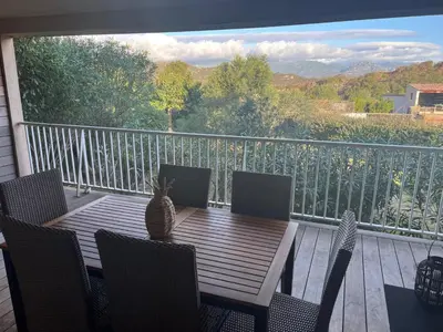 a wooden table and chairs on a balcony with a cat on it at Appartement & Piscine Santa Giulia in Porto-Vecchio