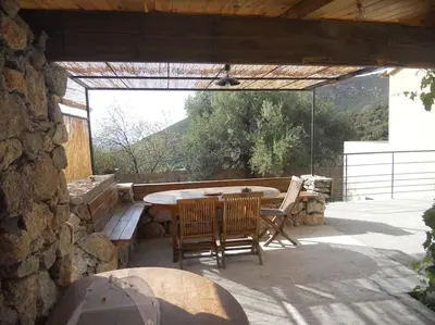 a patio with a table and chairs and a stone wall at SEJOUR DETENTE BALAGNE ENTRE MER ET MONTAGNE in Urtaca