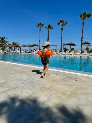 a woman in a hat carrying a life jacket next to a swimming pool at CASA MARE in Ghisonaccia