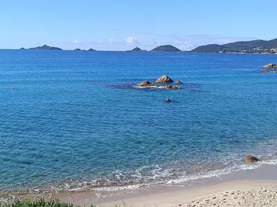 a beach with blue water and rocks in the ocean at chambre d'hôte cosy L'AGHJA in Carbuccia