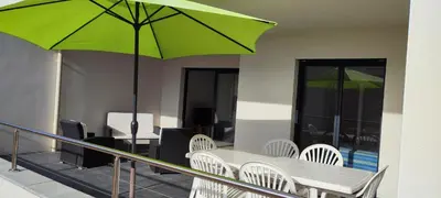 a table and chairs with a green umbrella on a balcony at Grand T2 neuf classé 3 étoiles in Porticcio