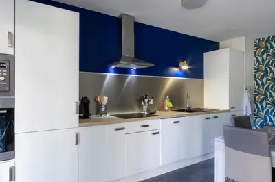 a kitchen with white cabinets and a blue wall at Le Petra - Appt climatisé proche de la plage in Ajaccio