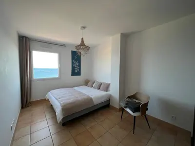 a bedroom with a bed and a window and a chair at Mini villa Hameaux des Sanguinaires AJACCIO in Ajaccio