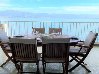 a table with chairs and wine glasses on a balcony at Appartement vue mer Carmino Ajaccio in Ajaccio