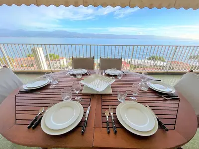 a wooden table with plates and wine glasses on a balcony at Appartement vue mer Carmino Ajaccio in Ajaccio
