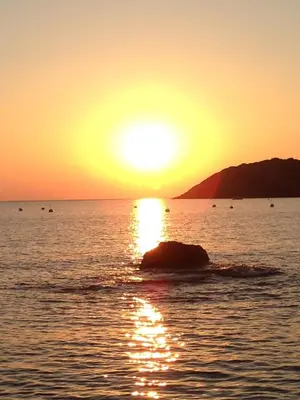a sunset over the ocean with a rock in the water at Villa SYMPHONY A PIANA CORSE DU SUD in Piana