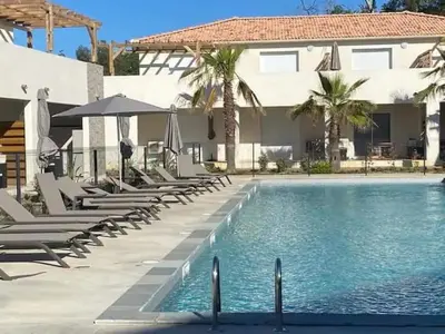 a pool with chairs and umbrellas next to a house at Superbe appartement vue mer terrasse couverte face à la mer in Linguizzetta