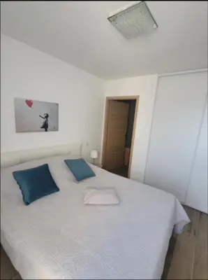 a white bed with blue pillows in a room at Appartement dominant la baie d'Ajaccio in Ajaccio