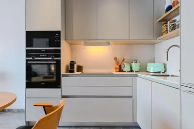 a white kitchen with white cabinets and a table at Le Galatée ,T2 luxe pieds dans l'eau in Porticcio