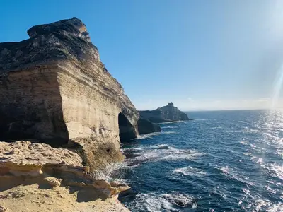 a rock cliff next to the ocean with a rainbow at Jolie maison individuelle dans l’extrême sud in Monacia-dʼAullène