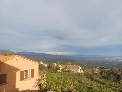 a house on a hill with mountains in the background at Cœur de village de charme in Sari Solenzara