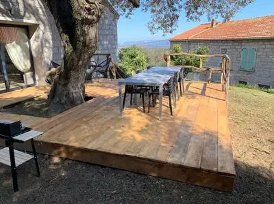 a table and chairs on a wooden deck under a tree at L'alivu di porto vecchio*** ( piscine chauffée ) in Porto-Vecchio