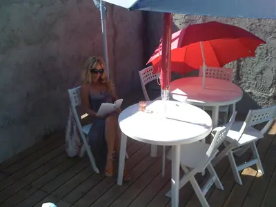 a woman sitting in a chair next to a table with an umbrella at maison T3 500m de la plage in Poggio-Mezzana