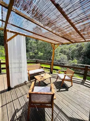 a wooden deck with a pergola and tables and chairs at Chalet au calme à Sagone en Corse in Sagone