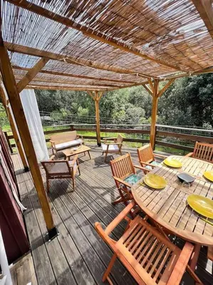 a wooden deck with a table and chairs and a pergola at Chalet au calme à Sagone en Corse in Sagone