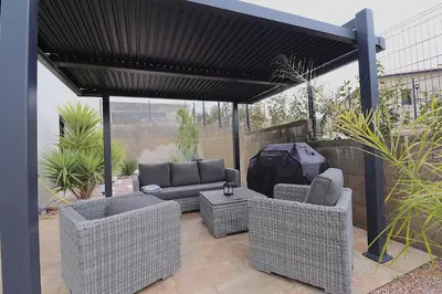 a patio with wicker furniture and a black canopy at La Maison de vacances à Ajaccio- Proche plage et aéroport- Extérieur privatif avec barbecue in Ajaccio