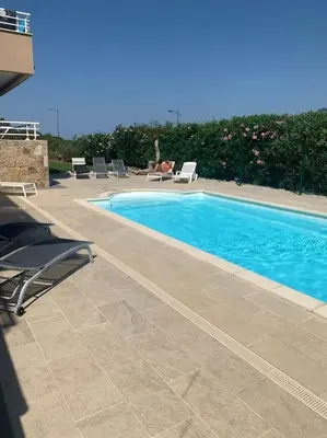 a swimming pool with chairs and a person sitting next to it at Grand appartement T4 - piscine - vue féérique in Propriano