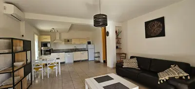 a living room with a black couch and a kitchen at T2 Paisible Quartier Vigna Majo, Olmeto in Olmeto