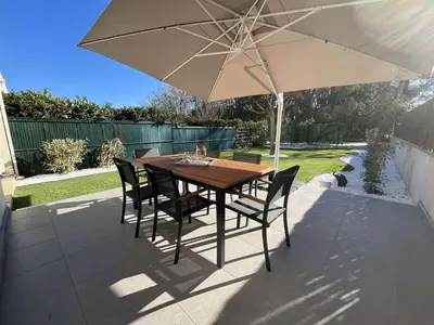 a table and chairs under an umbrella on a patio at Appartement jardin à deux pas de la mer Classé 3 étoiles in Poggio-Mezzana