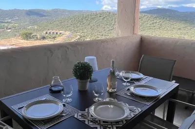 a table with plates and wine glasses on a balcony at Appartement 4 pers vue sur la baie de Santa Giulia in Porto-Vecchio