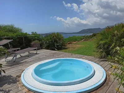 a blue tub on a wooden deck with a view of the water at Villa classée 5* 7 chambres piscine spa plage à 5' in Sainte-Lucie de Porto-Vecchio