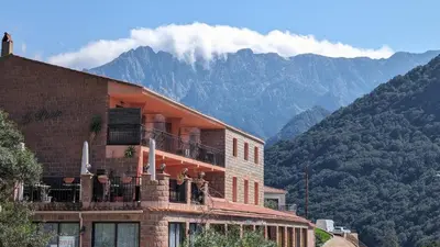 a building with a balcony with mountains in the background at Le Porto T3 55m2 vue mer immeuble traditionnel en pierre de taille avec prestations exceptionnelles barbecue ordinateur vidéosurveillance terrasse panoramique in Porto Ota