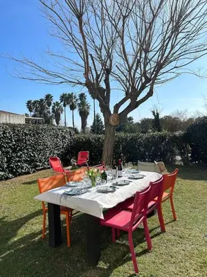 a table with red chairs around it with a tree at Rez de Jardin Piscine et Plage in Poggio-Mezzana