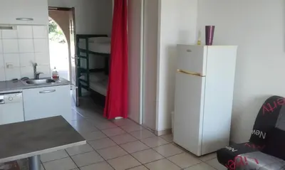 a kitchen with a white refrigerator and a red curtain at Haute Corse. Studio 4 pers .Plage Piscine. Cervione Prunete . in Cervione
