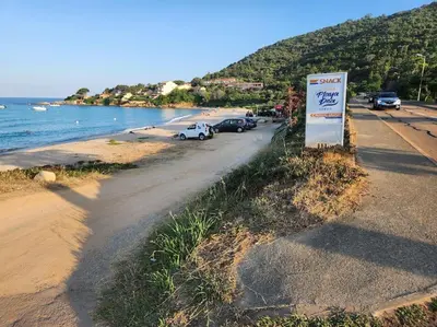 a sign next to a beach with cars parked at Pieds dans l'eau - La Villa Crique aux tortues in Zonza