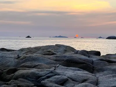 a group of rocks in the ocean with the sun in the background at Casa Mare, CABANON SUR LA PLAGE à Ajaccio vue sanguinaires in Ajaccio