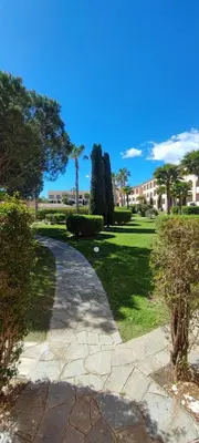 a walkway through a park with trees and a building at appartement bord de mer en Corse avec 2 piscines 100 metres de la plage in Linguizzetta