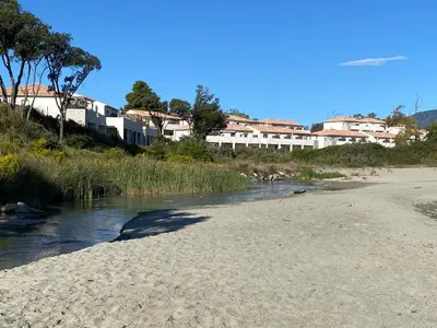 a beach next to a river with buildings in the background at Studio en bord de mer sur Costa Serena N54 in Linguizzetta