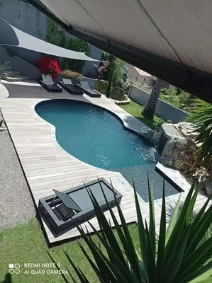 a swimming pool with a table and chairs on a wooden deck at Appartement F2 dessous de villa in Olmeta-di-Tuda