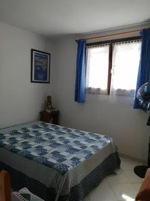 a bedroom with a bed and a window with blue curtains at Maison près de la plage in Penta-di-Casinca