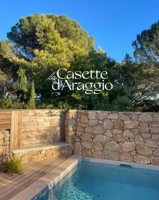 a swimming pool with a stone wall and a sign at Locations de La Casette d'Araggio in Porto-Vecchio