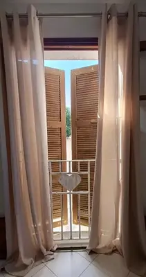 a window with curtains and a chair on a balcony at Entre mer et montagne in Monte