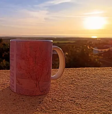 a red coffee mug sitting on a table with the sunset at Entre mer et montagne in Monte