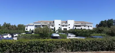 a large white building with cars parked in a parking lot at Appartement T3 les pieds dans l'eau in Moriani Plage