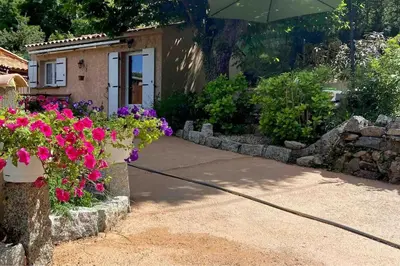 a house with flowers and an umbrella in front of it at Mini villa de charme. in Zonza