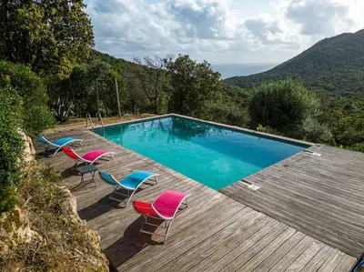 a swimming pool with chairs and a wooden deck at Maison vue Mer et Maquis in Olmeto