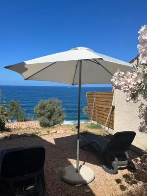 a white umbrella and a chair and a chair and a chair at Appartement bord de mer 2 personnes in Sagone